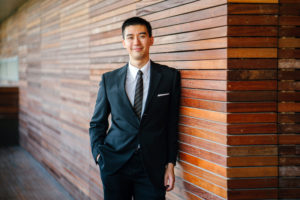 man wearing suit leaning against brick wall