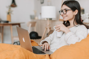 student sitting on sofa with laptop and cup