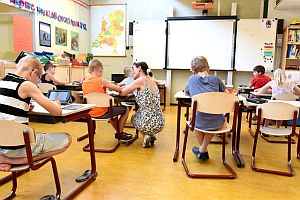 teacher bent over working with a student at their desk in a classroom