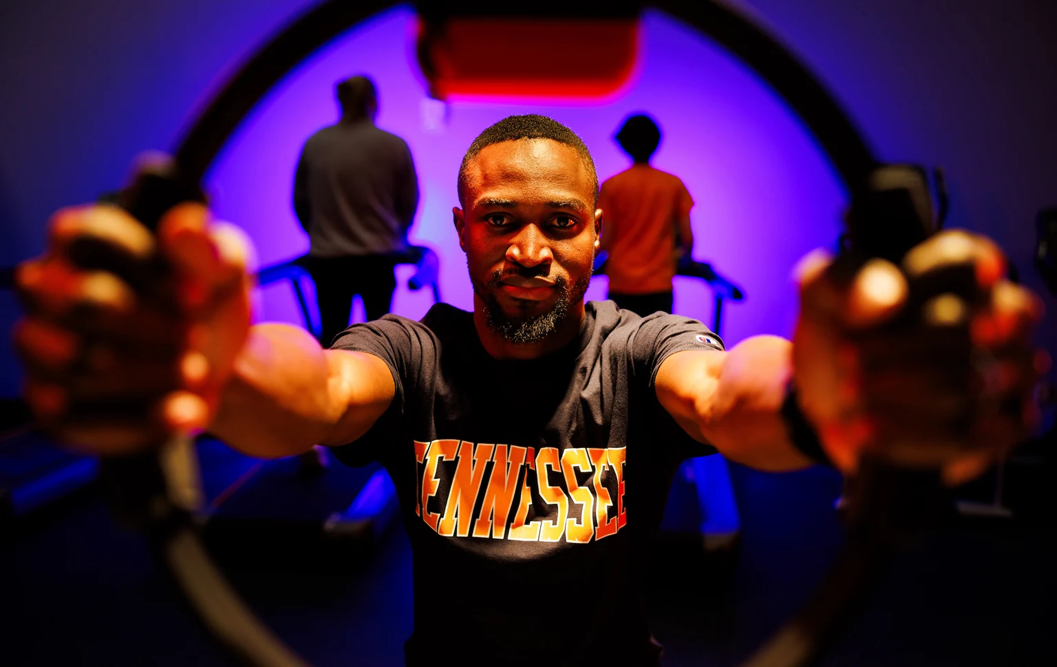KRSS student in a Tennessee shirt holding resistance bands toward the camera in a fitness lab lit in purple
