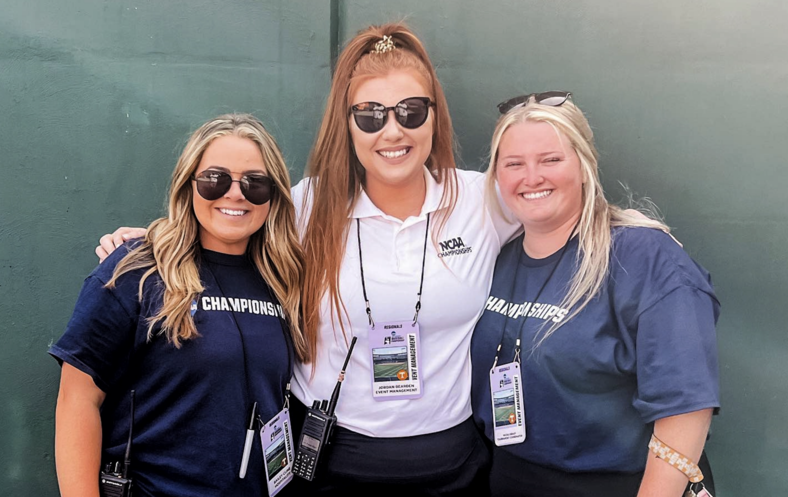 Three sport management students working an NCAA championship event, wearing staff credentials