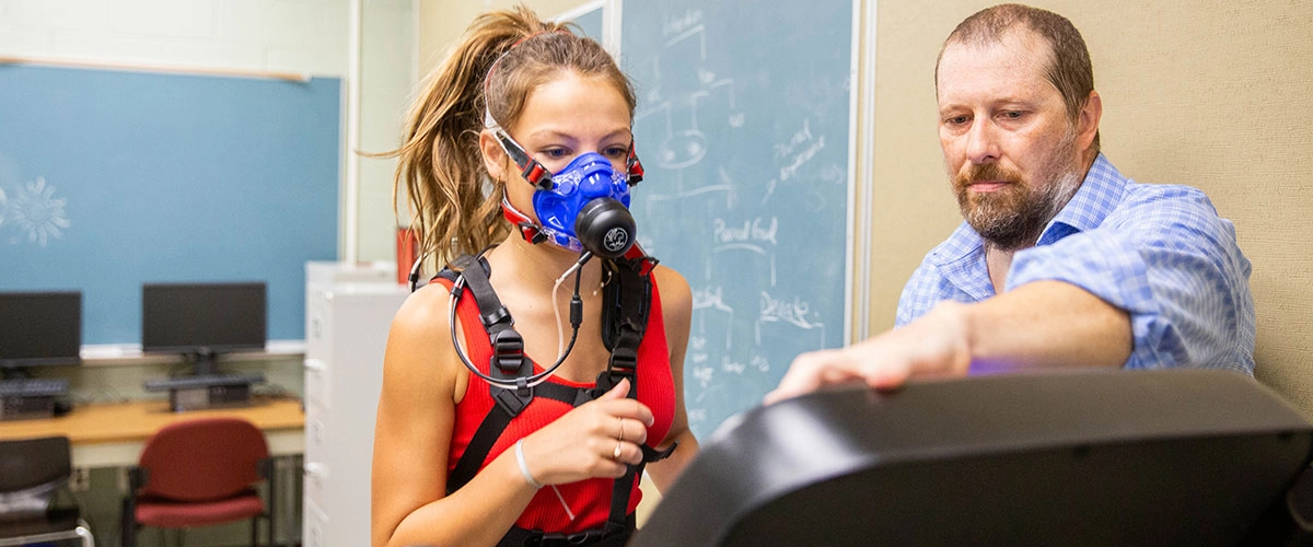 Researcher adjusting a treadmill as a student wears a metabolic mask during an exercise test