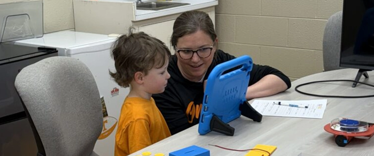 Researcher working with a young child on a tablet activity in the Move + Play Lab