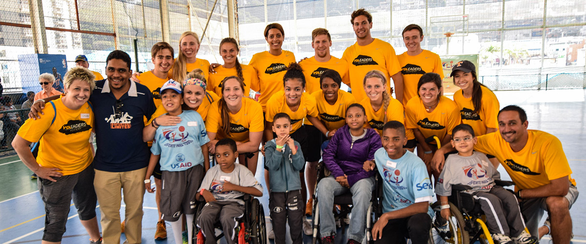 Dr. Sarah Hillyer and VoLeader students stand for a group photo while wearing matching orange tshirts. Children from the event stand or sit in wheelchairs with them.