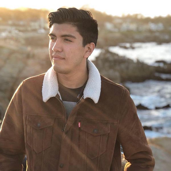 Rob Ruiz stands in front of an ocean coast line looking into the distance.