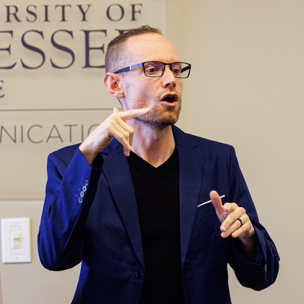 Photo of Calvin Farley wearing a dark blue blazer signing in a classroom while teaching.