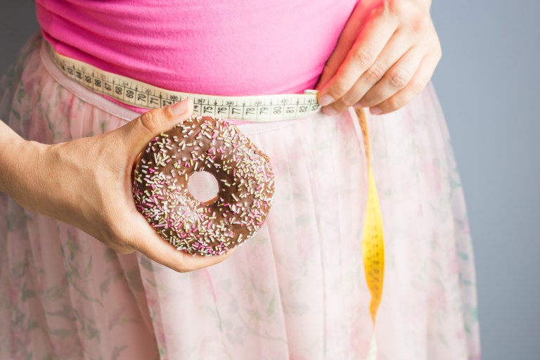 person holding doughnut while measuring waistline