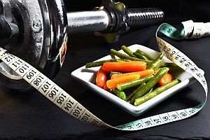 plate of healthy vegetables, measuring tape, and hand weight