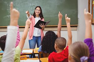 teacher in front of classroom of students whith hands raised