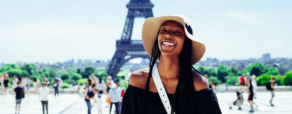 A Black woman smiles at the camera with the Eiffel Tower behind her