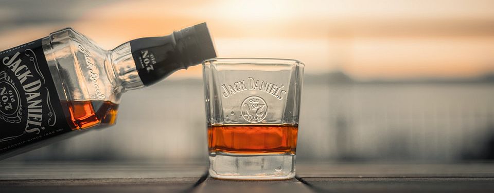 Jack Daniels being poured from labeled bottle into engraved shot glass on counter
