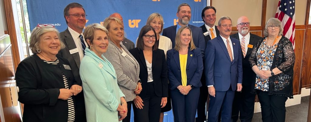 Ellen McIntyre, Donde Plowman, David Cihak, and other stakeholders from the university stand together for a photo in front of the UT System's backdrop.
