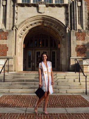 Lily Deinhart wearing her sash and holding her graduation cap while standing in front of Ayres Hall