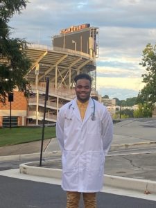 Photo of Bryson Hartsell wearing while lab coat and standing in front of Neyland Stadium on the University of Tennessee, Knoxville campus