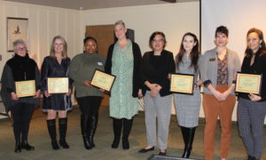 Group of eight women holding up award plaques.