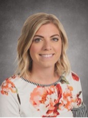 Portrait photo of Bethany Saunders. She has fair skin and blonde hair. She is wearing a floral print shirt and is smiling in the photo.