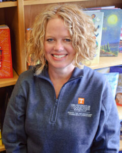 Susan GROENKE. Feminine presenting white person with short curly blond hair smiling at the camera wearing a dark grey UT Knoxville pullover.