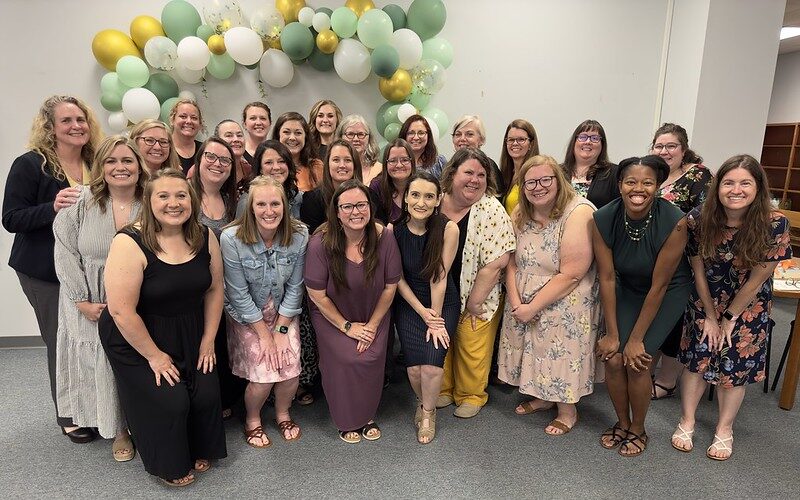 Photo of the Literacy Specialist graduates and faculty. They are in front of a balloon sculpture and all are smiling in the photo. The group is made of women and they are smiling for the photo.
