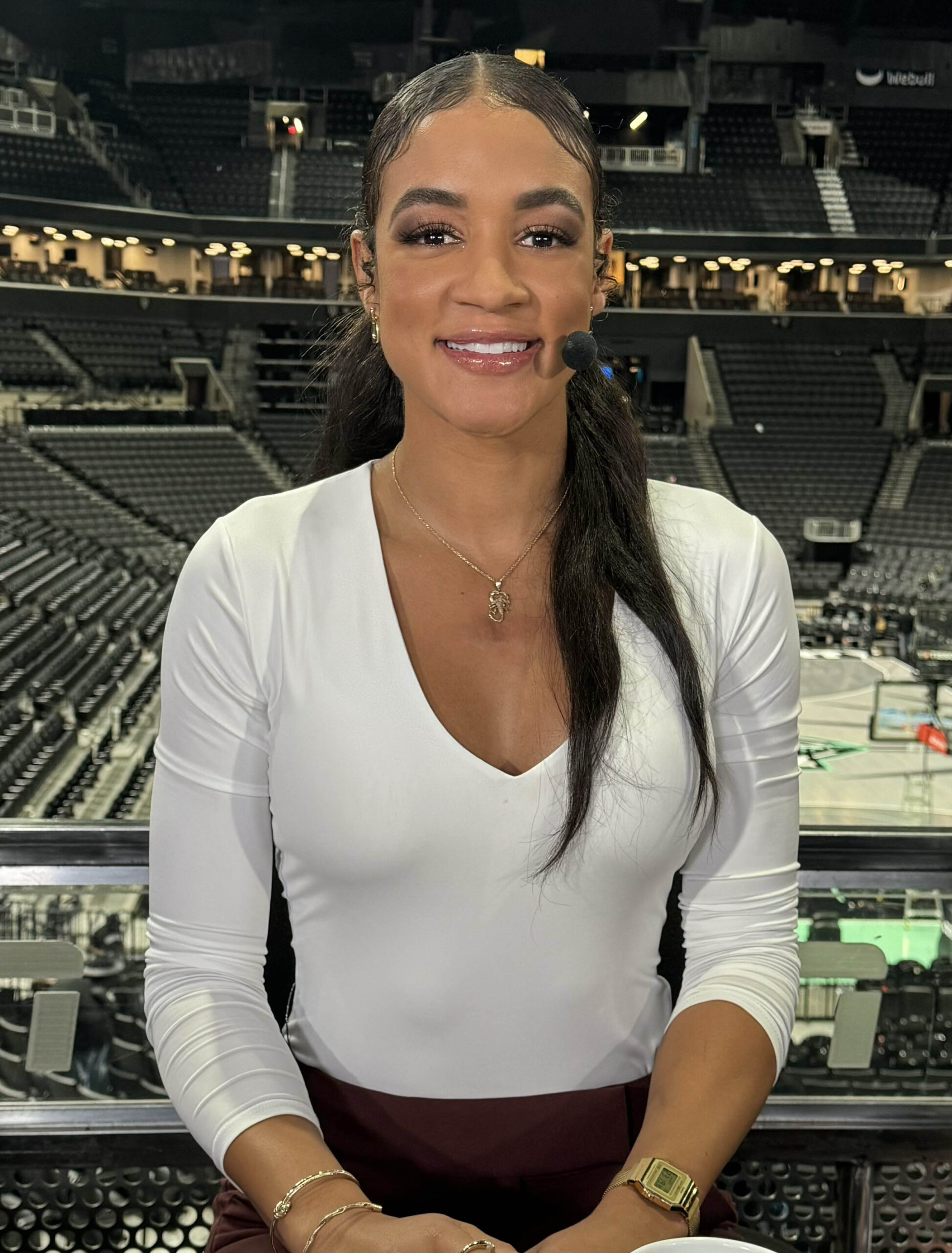 Andraya Carter is sitting in an arena preparing for a broadcast. She has dark skin and black hair. She is smiling in the photo. 