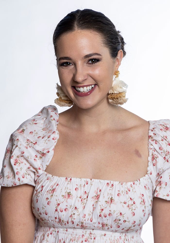 Portrait photo of Mary Cayten Brakefield. She has fair skin and dark hair. She is wearing a floral dress and is smiling in the photo