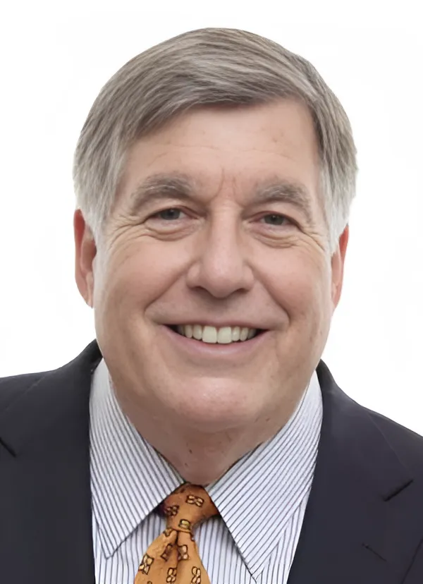 Portrait of Bob Kesling—a man with light skin and short gray hair—wearing a striped button-down shirt, an orange tie, and a black blazer, against a white background.