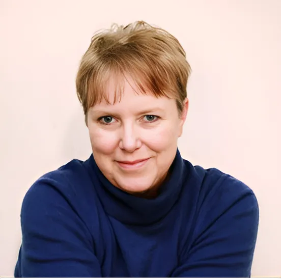 Portrait of Marcia Goldenstein—a woman with light skin and a short dark blonde pixie cut—wearing a navy turtleneck against a simple background.